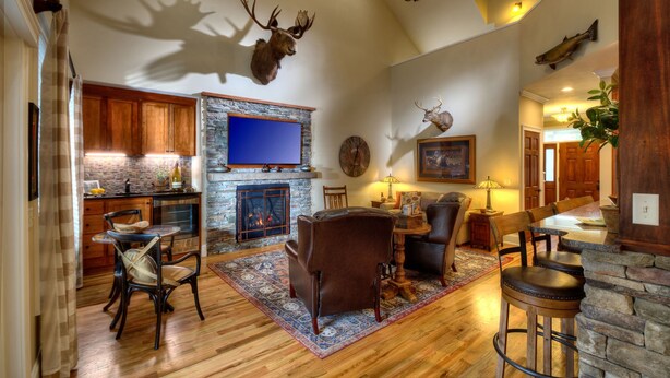 A spacious living room with a fireplace, a stone wall, and a mounted deer head.