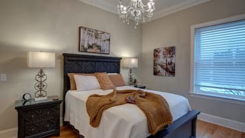 Une chambre à coucher avec un lit, deux tables de chevet, un lustre et des œuvres d’art accrochées aux murs.