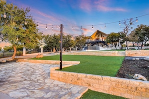 A landscaped outdoor area with a stone pathway, a grassy lawn, and a brick retaining wall. - Lake Front Home with Pool, Dock, Views, Sports Court, & Beautiful Sunsets! (Lago Vista)