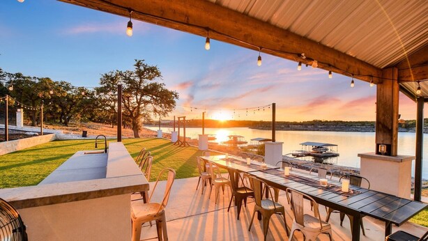 An outdoor dining area with a view of a lake and sunset. - Lake Front Home with Pool, Dock, Views, Sports Court, & Beautiful Sunsets! (Lago Vista)