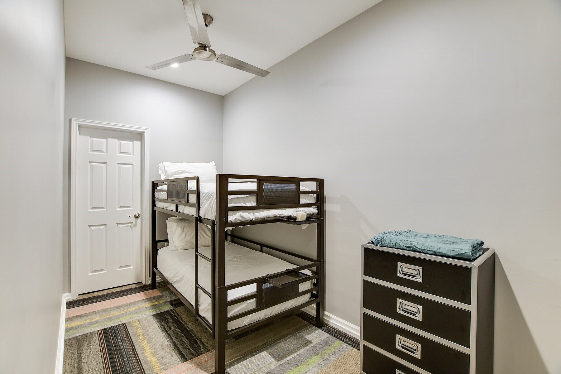A bunk bed with a ceiling fan, a white door, and a storage unit with drawers.
