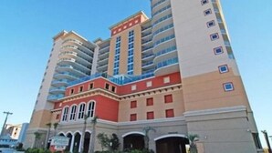 A multi-story hotel with a central red and beige facade, balconies on each floor, and a clear sky. - Units at Atlantic Breeze by Elliott Beach Rentals (North Myrtle Beach)