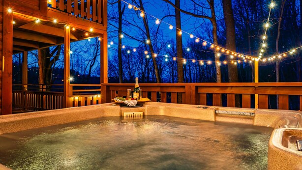A hot tub area with string lights, wooden deck, and a view of trees. - The Hilltop Chalet : Location, Views, Hot tub, Fire Pit, Game Room! (Gatlinburg)