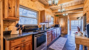 A wooden cabin kitchen with a large stove, wooden cabinets, and a dining area with a table and chairs. - The Hilltop Chalet : Location, Views, Hot tub, Fire Pit, Game Room! (Gatlinburg)