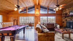 A wooden cabin interior with a pool table, a sofa, a fireplace, and a stone wall. - The Hilltop Chalet : Location, Views, Hot tub, Fire Pit, Game Room! (Gatlinburg)