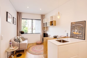 A modern kitchen with a sink, a small dining area with a table and chairs, a sofa with cushions, a round rug, and a window with curtains.