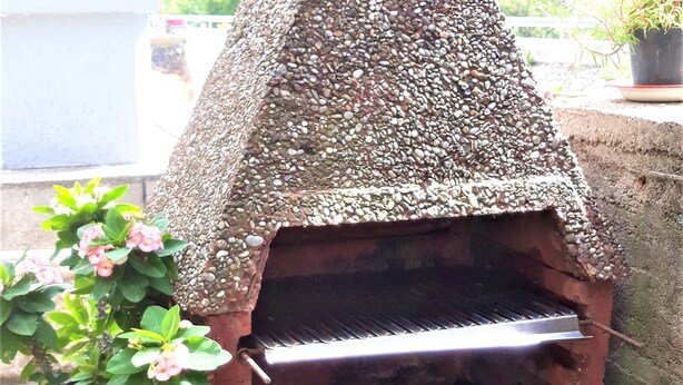 Forno de tijolos ao ar livre com chaminé de pedra, planta em vaso e um recipiente metálico abaixo.