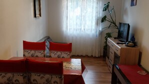 Quarto com mesa de jantar e cadeiras, televisão em uma cômoda e uma planta.