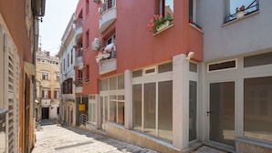 A narrow street with buildings on either side, featuring balconies with potted plants and a clear sky. - Luxury apartment Vivaldi - Two bedroom apartment (Pula)