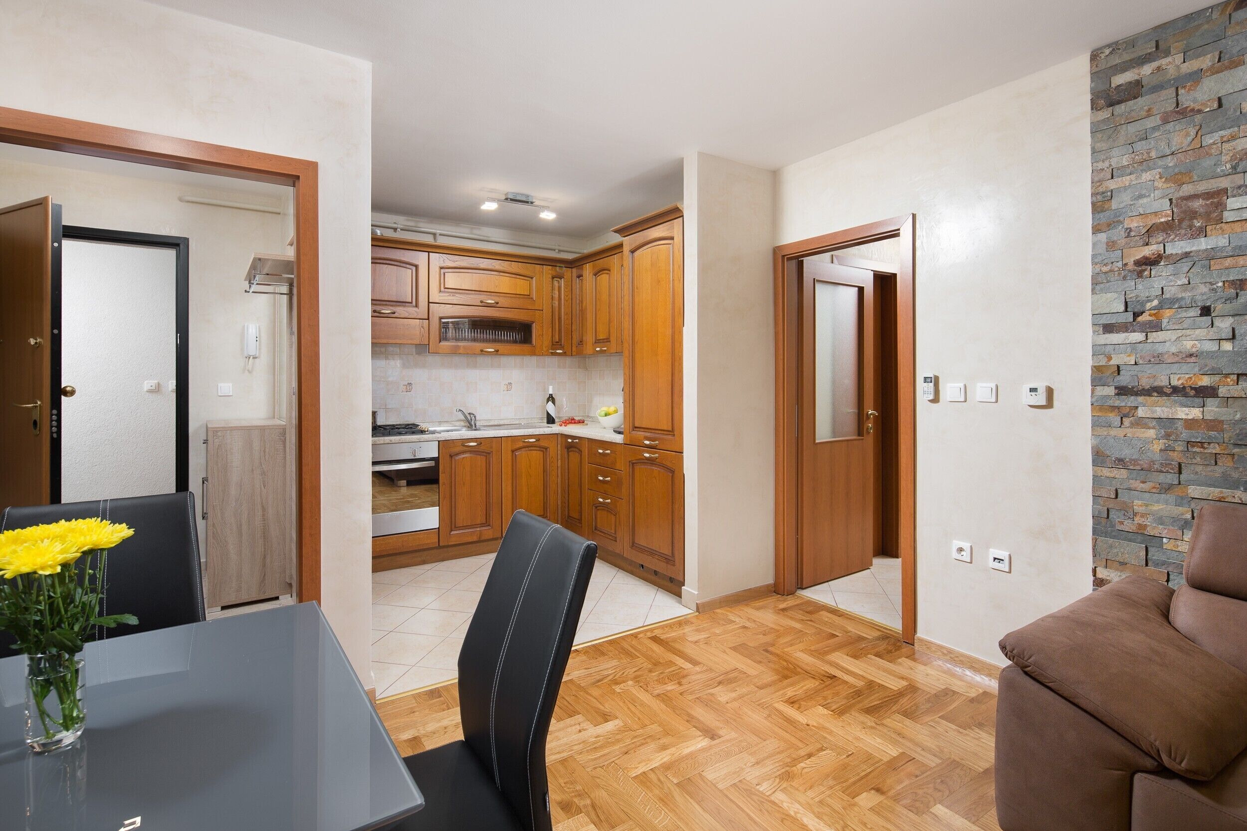 A modern kitchen with wooden cabinets, a dining area with a table and chairs, and a stone accent wall.