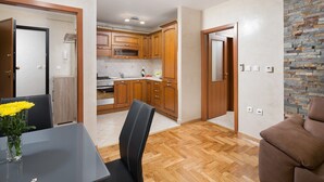 A modern kitchen with wooden cabinets, a dining area with a table and chairs, and a stone accent wall. - Luxury apartment Vivaldi - Two bedroom apartment (Pula)