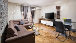 A modern living room with a brown sofa, a glass coffee table, a TV, and a dining area with chairs and a table. - Luxury apartment Vivaldi - Two bedroom apartment (Pula)