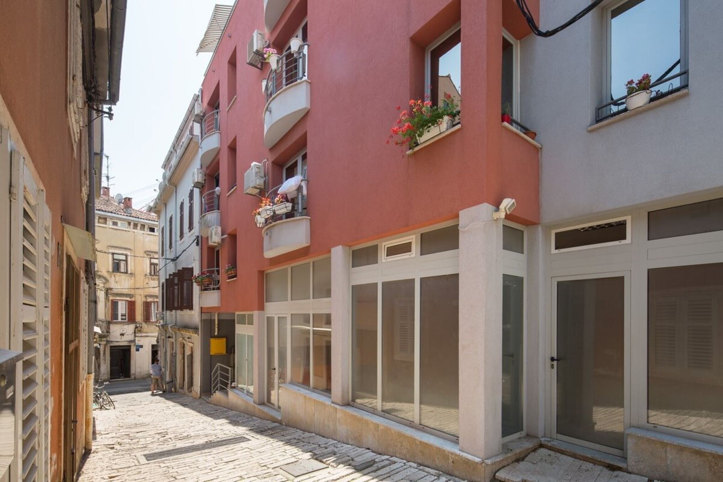 Une ruelle étroite pavée, bordée d’immeubles à plusieurs étages dotés de balcons, de grandes fenêtres et présentant un mélange de styles architecturaux.