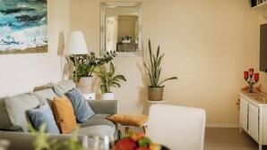 En stue med sofa, spisebord med frugtskål og plantekrukker.