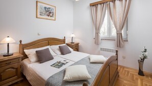 Ein ordentlich eingerichtetes Schlafzimmer mit einem hölzernen Bett, Nachttischlampen, einem gerahmten Bild an der Wand und einem Fenster mit Vorhängen.