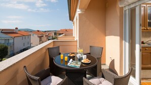 Ein Balkon mit Korbmöbeln, einem Tisch mit Frühstücksangeboten und Blick auf Gebäude im Hintergrund.