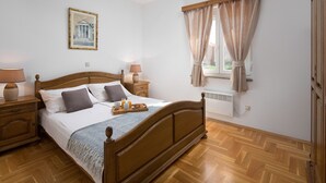 A neatly arranged bedroom with a wooden bed, bedside lamps, a framed picture on the wall, and a window with curtains.