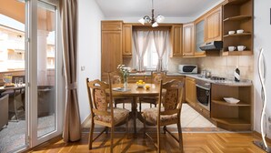 A modern kitchen with wooden cabinets, a dining table with floral chairs, and a view of the balcony.