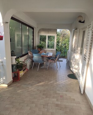 Eine sonnendurchflutete Terrasse mit Tisch und Stühlen, Blumentöpfen und Blick ins Grüne.