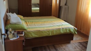 Une chambre à coucher comprenant un lit, une armoire en bois, une table de chevet et un miroir.