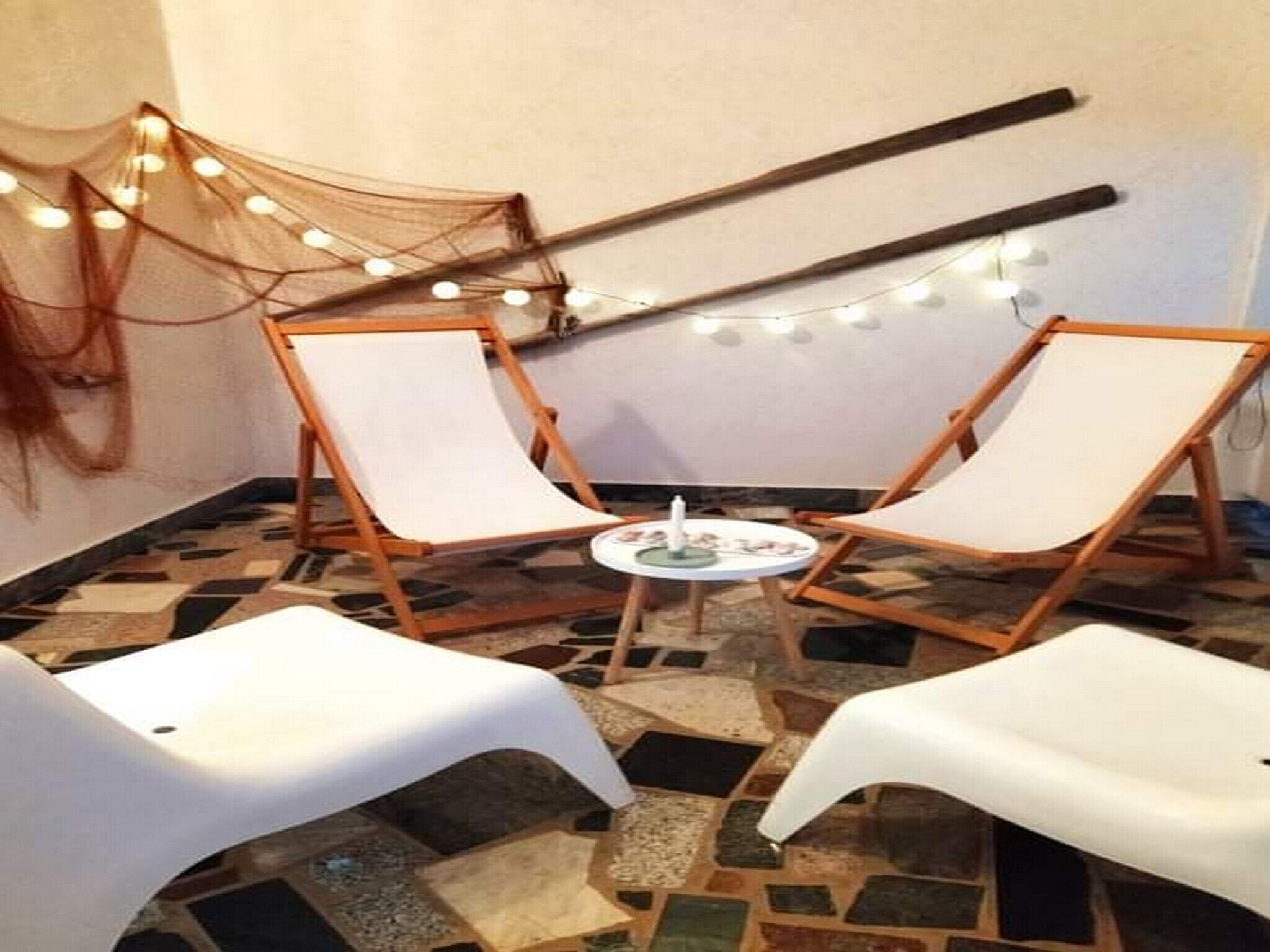A room with two white lounge chairs, a small round table, and string lights on the wall.