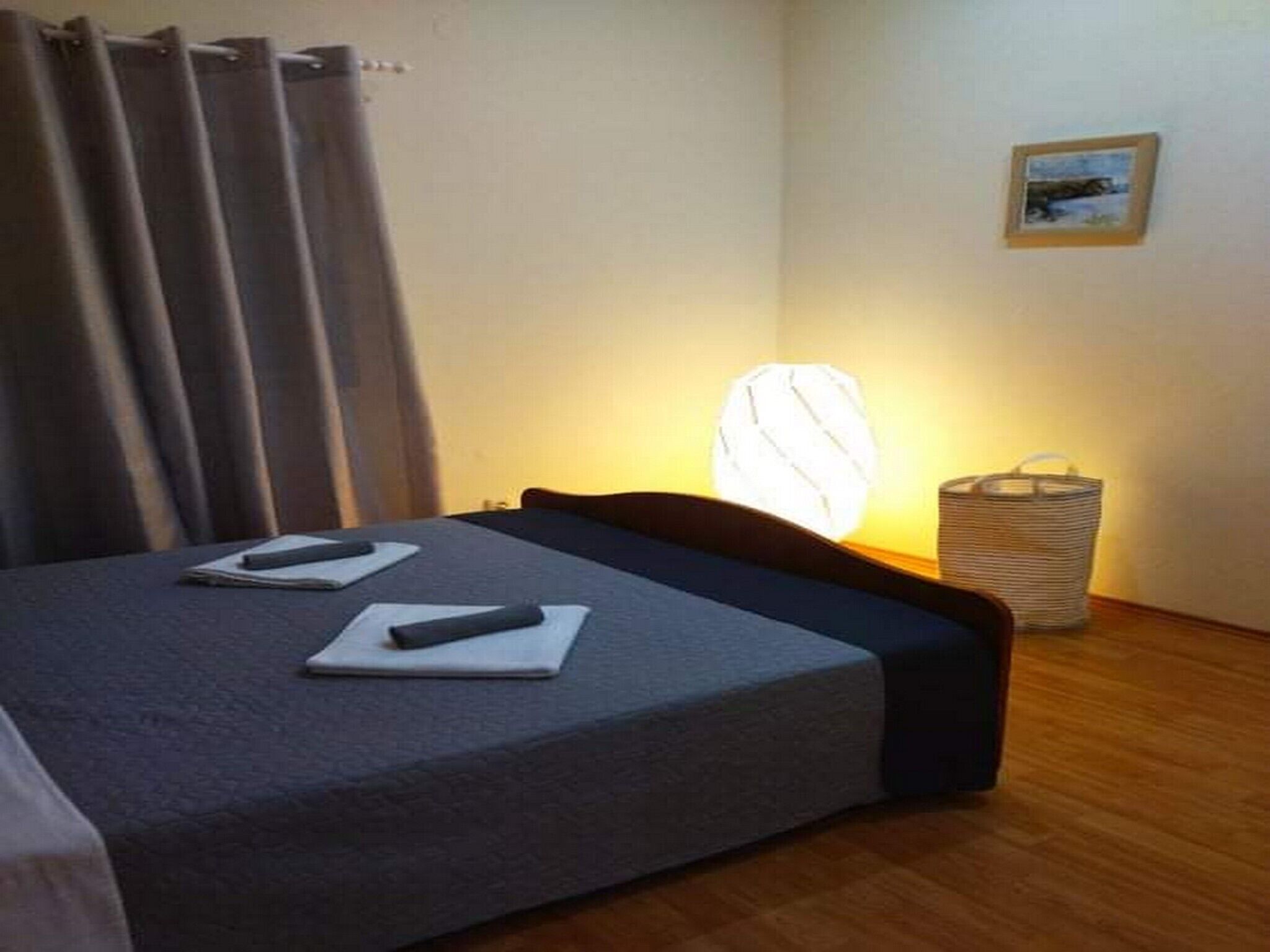 Una habitación de hotel con una cama, una mesita de noche con una lámpara, una cesta pequeña y un cuadro en la pared.