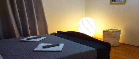 Una habitación de hotel con una cama, una mesita de noche con una lámpara, una cesta pequeña y un cuadro en la pared.