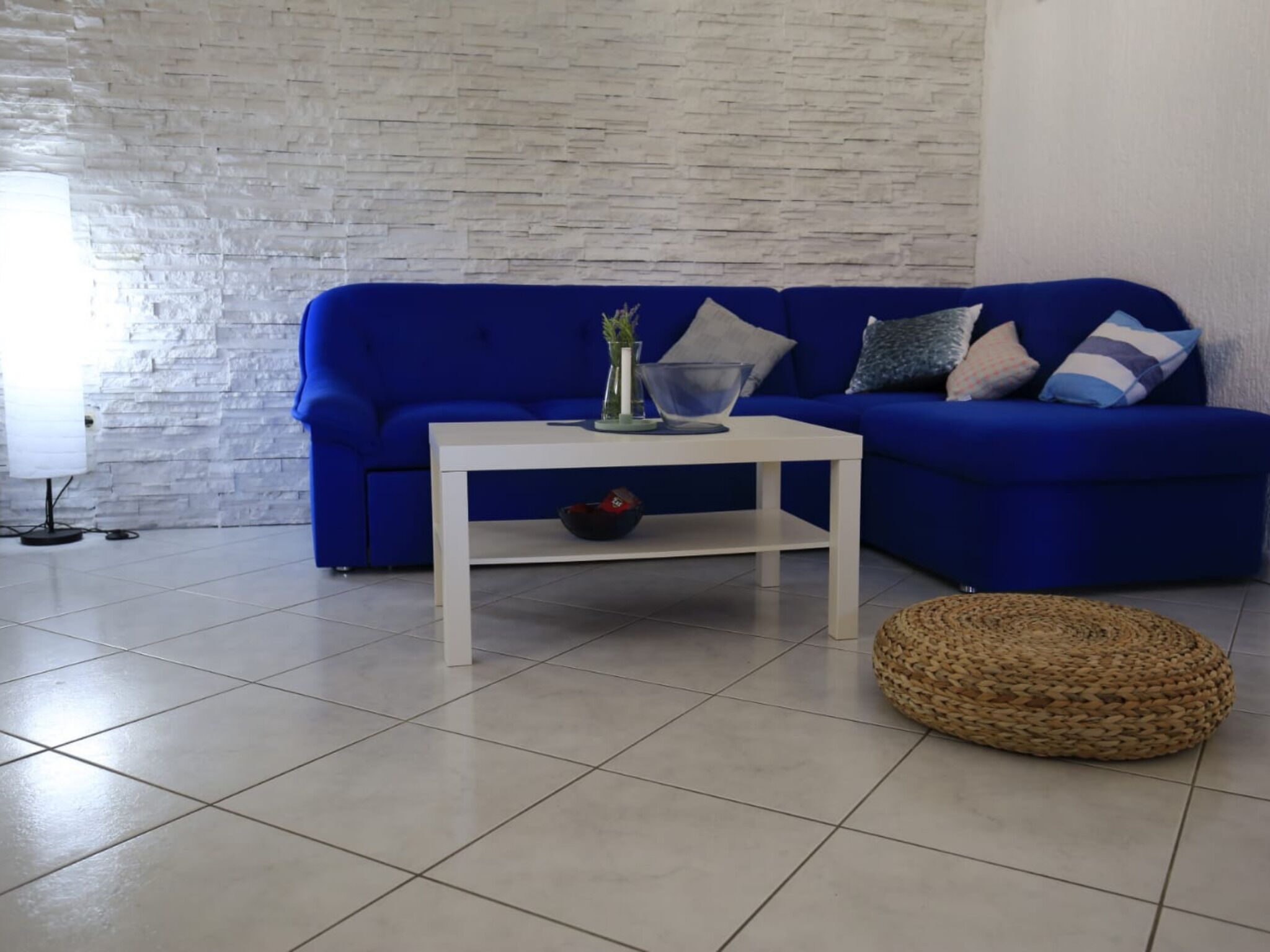 A living room with a blue sofa, a white coffee table, and a woven ottoman.