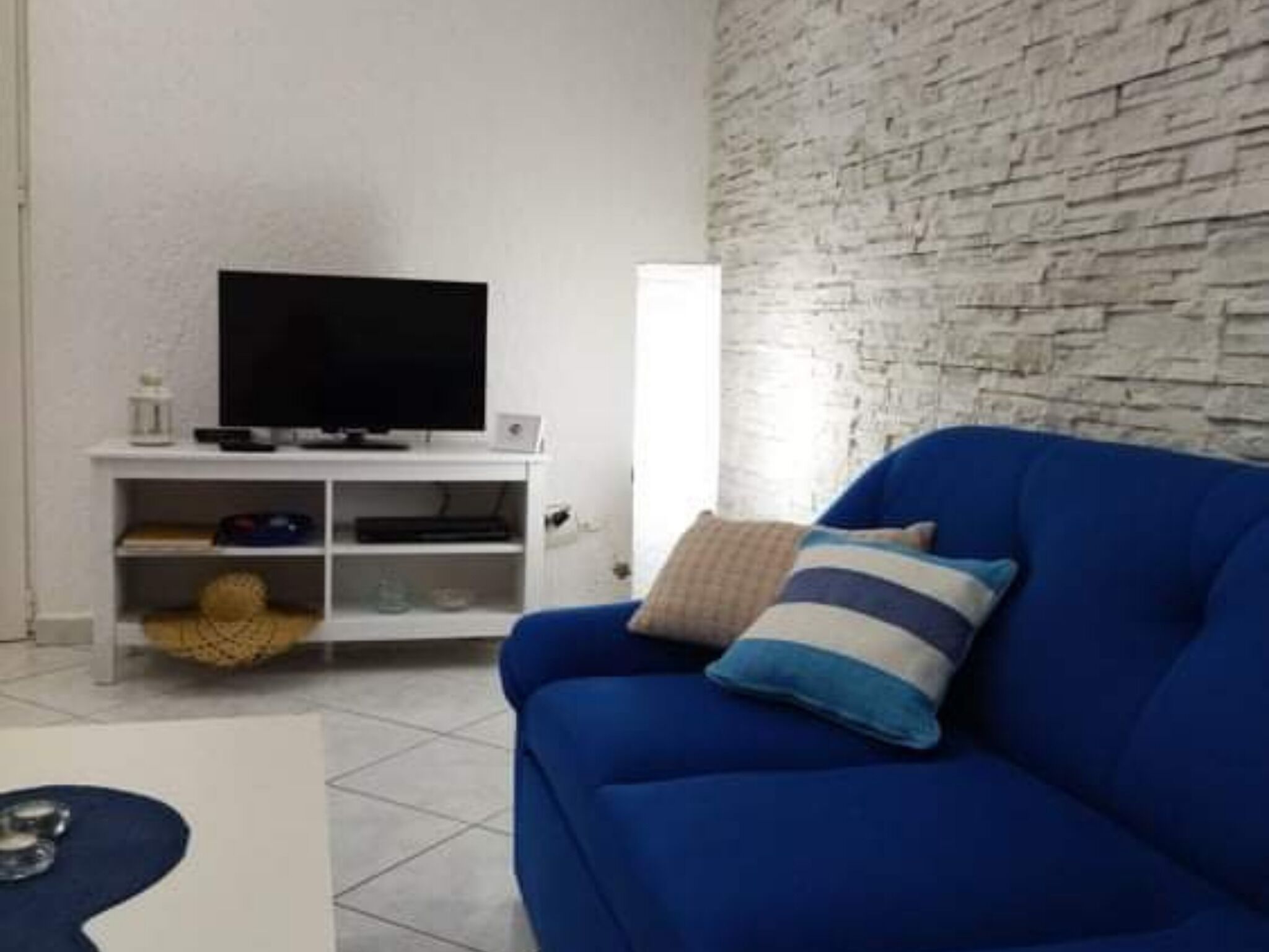 A living room with a blue sofa, a television on a white stand, and a textured wall.
