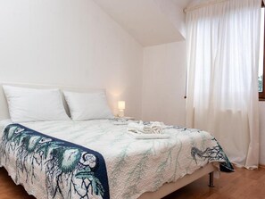 A bedroom with a bed, white curtains, and a nightstand with a lamp.