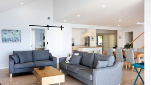 Een moderne woonkamer met twee grijze banken, een houten salontafel en een eethoek met een houten tafel en stoelen.