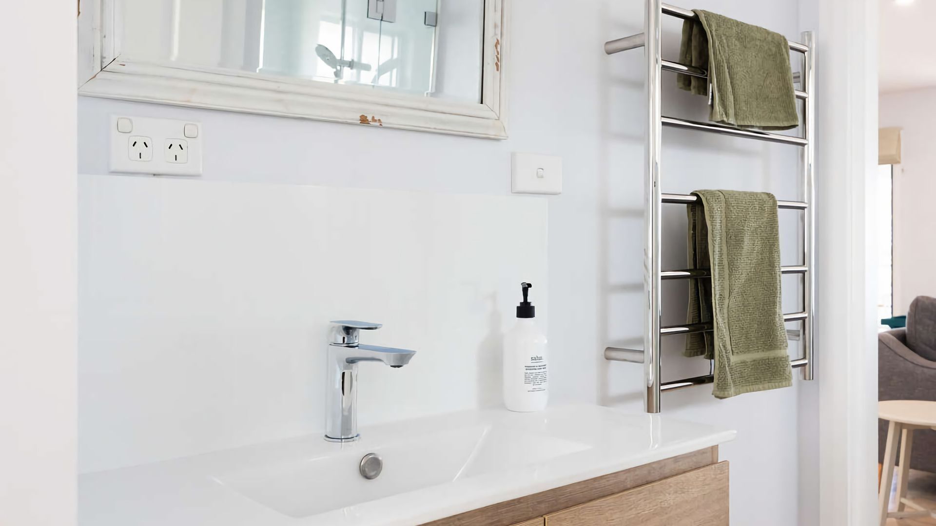 Une salle de bain avec un lavabo blanc, un robinet chromé et un porte-serviettes sur lequel est posée une serviette verte.