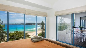 Een slaapkamer met een groot raam met uitzicht op een strand en een balkon met buitenmeubilair.
