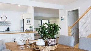 Een eetgedeelte met een houten tafel, witte borden, wijnglazen, een geweven mand en een potplant.