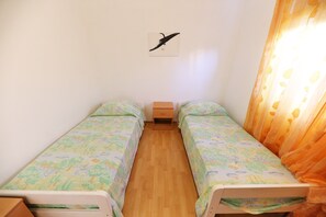 A small, single-room bedroom with two single beds, a wooden floor, a small bedside table, and a wall-mounted artwork. - Apartments Melita - Two Bedroom Apartment with Terrace and Sea View (Zadar)