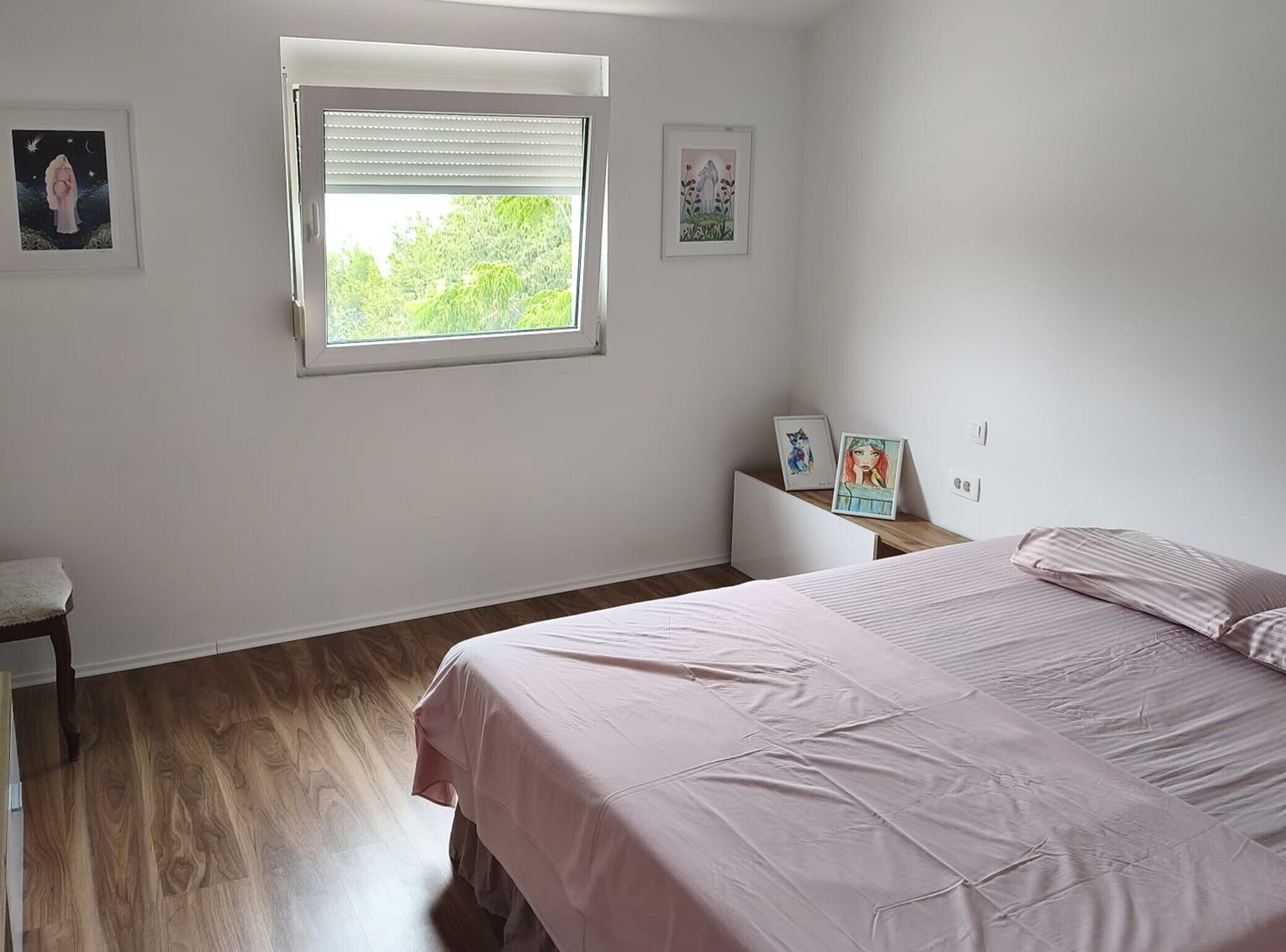 A bedroom with a bed, a window, and artwork on the walls.