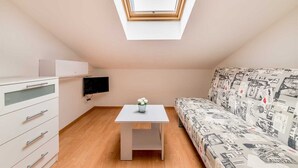 A small, modern room with a skylight, a white sofa with a graphic print, a white TV on the wall, and a small table with a plant. - Nikolina Bon Bon Happy Stay Center – Studio with Terrace & Sea view (Baška)