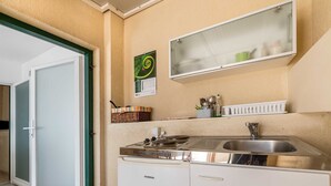 A compact kitchen with a sink, stove, and a small refrigerator. A calendar and a mirror are mounted on the wall. - Nikolina Bon Bon Happy Stay Center – Studio with Terrace & Sea view (Baška)