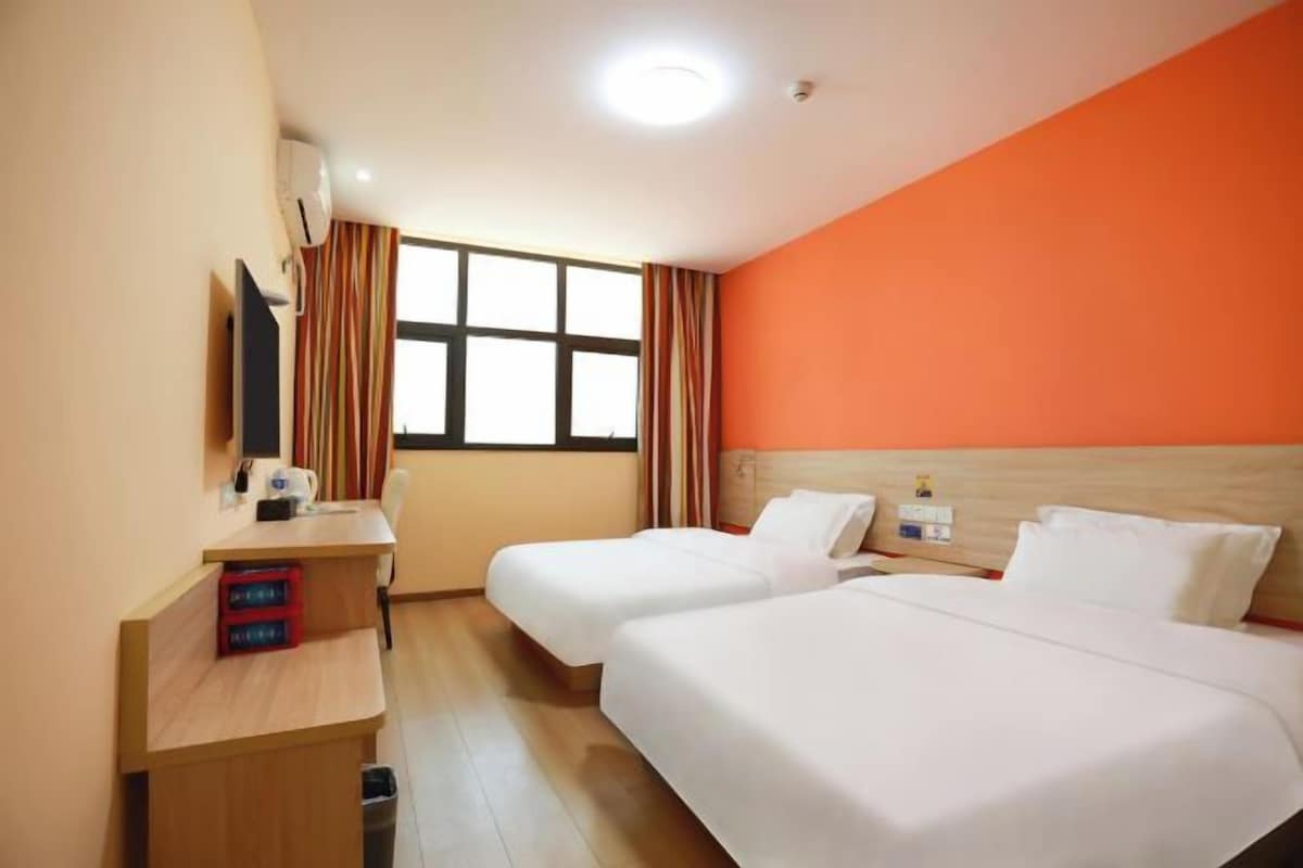 A hotel room with two beds, a desk, a TV, and a window with curtains.