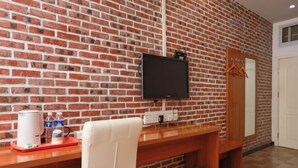 Habitación con pared de ladrillo, un televisor de pantalla plana montado, un escritorio de madera con una silla y un espejo.