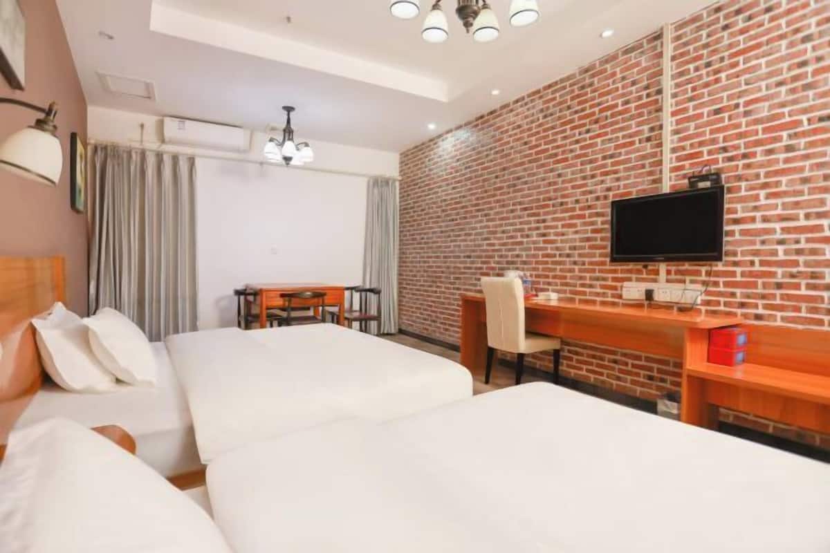 A hotel room with two beds, a desk, a television, and a brick wall.