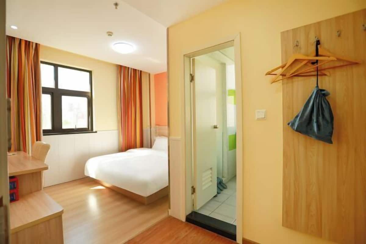 A hotel room with a bed, a desk, a window with curtains, and a door leading to a bathroom.