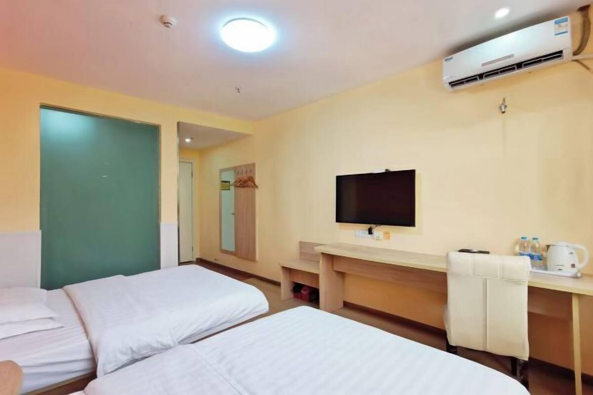 A hotel room with two beds, a desk, a chair, a TV, and an air conditioning unit.
