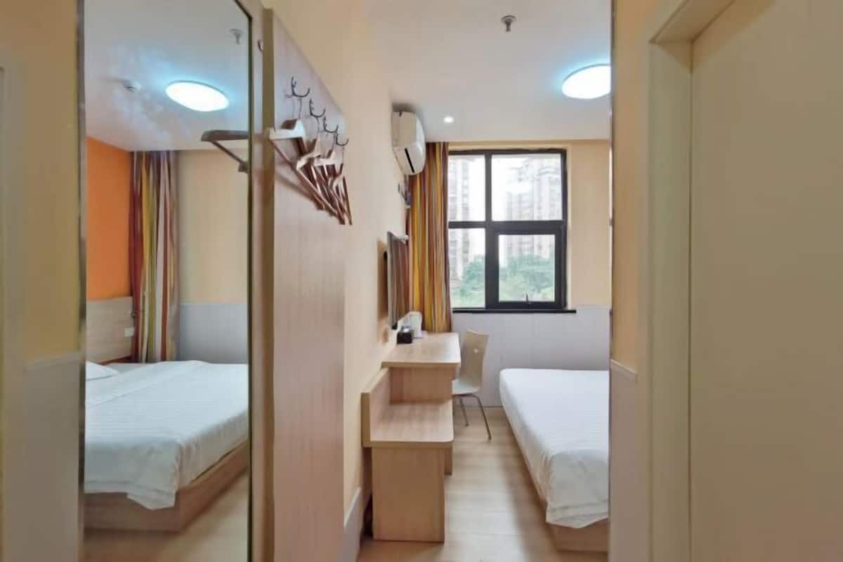 A hotel room with two beds, a desk, and a window with a view of buildings.
