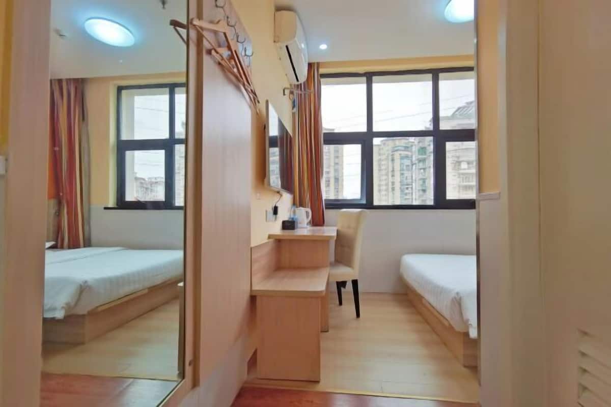 A compact hotel room with two single beds, a small desk, a chair, and a large mirror.