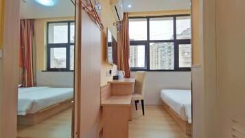 A compact hotel room with two single beds, a small desk, a chair, and a large mirror.