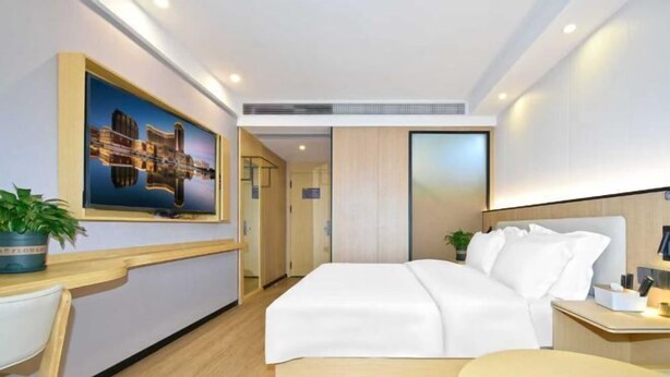 Una habitación de hotel moderna con una cama grande, un escritorio y una silla. Hay un cuadro en la pared y una planta en el escritorio.