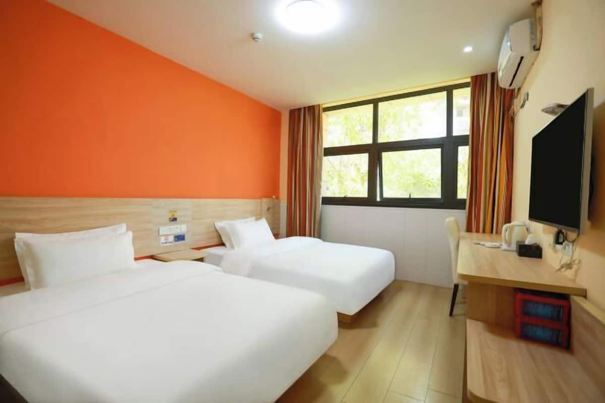 A hotel room with two beds, a desk, a TV, and a window with curtains.