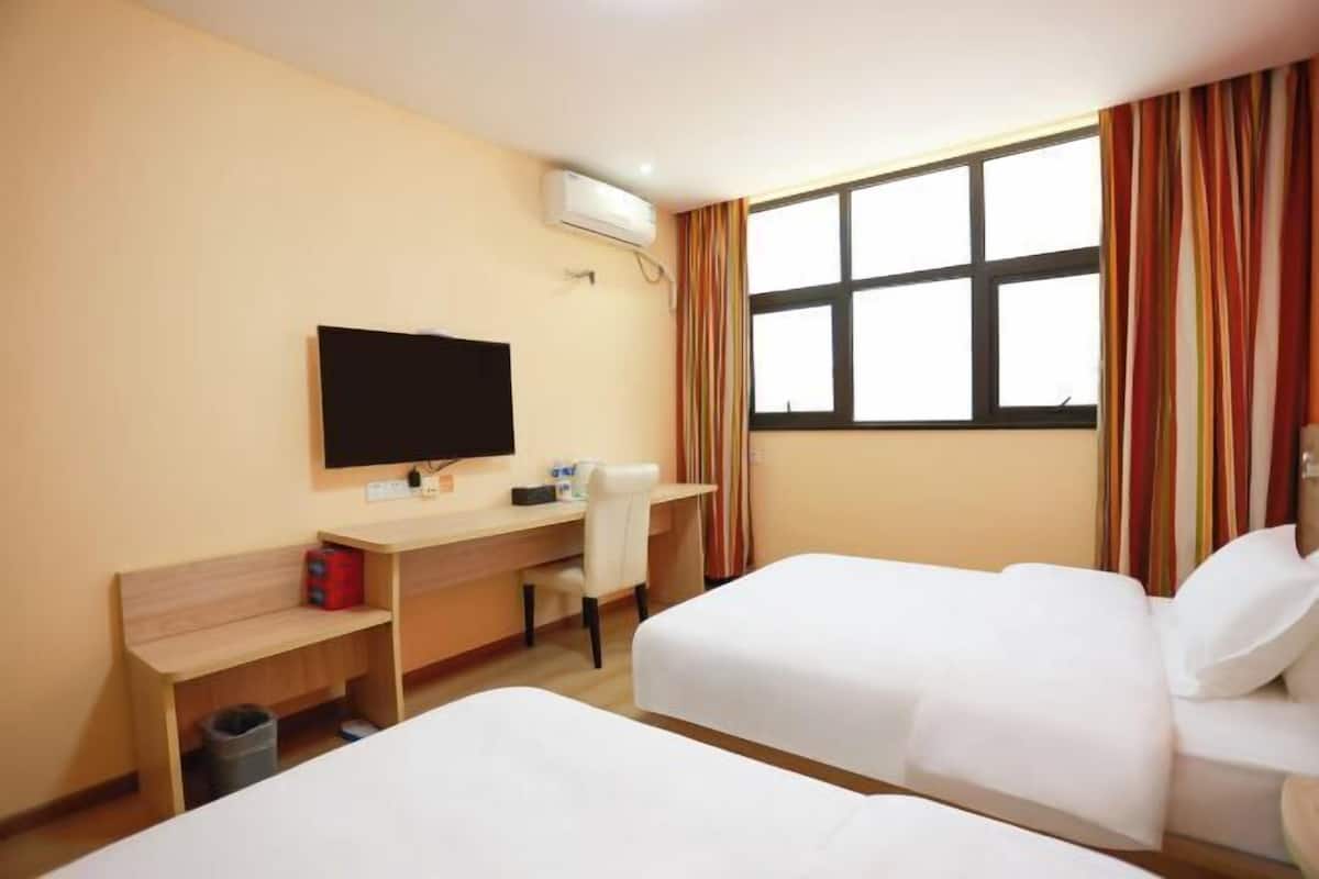 A hotel room with two beds, a desk with a chair, a television, and a window with curtains.