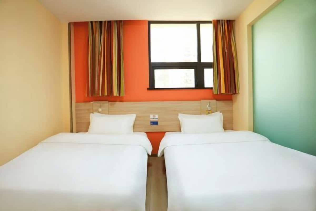 A hotel room with two beds, a window with curtains, and a wooden headboard.